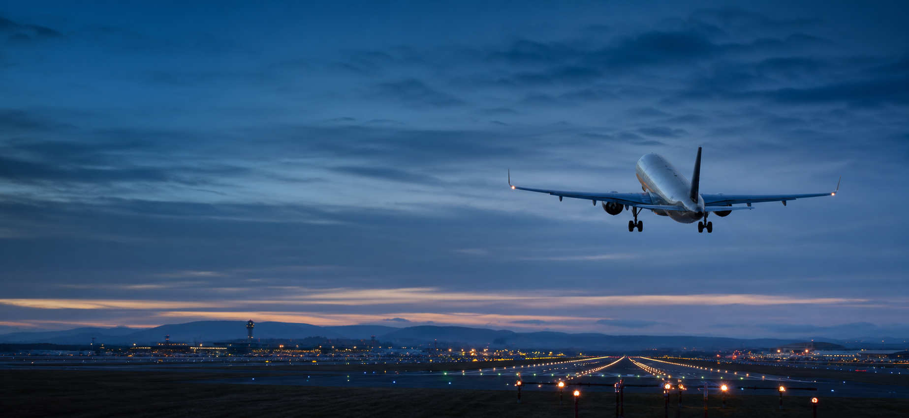 A commercial passenger aircraft taking off over an illuminated airport runway at blue hour